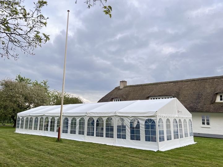 Langt festtelt med buede vinduer ved et stråtækt hus