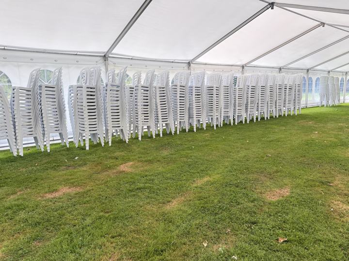 Stablede hvide plaststole klar i et festtelt på græs