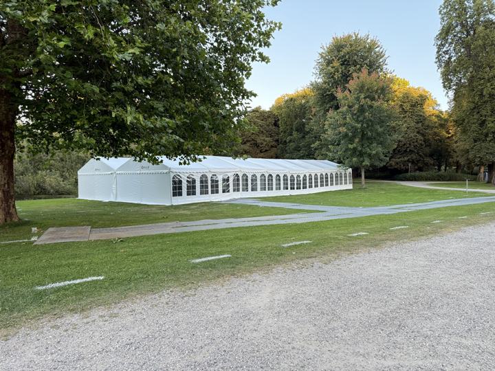 Langt hvidt festtelt med buede vinduer stillet op i en park